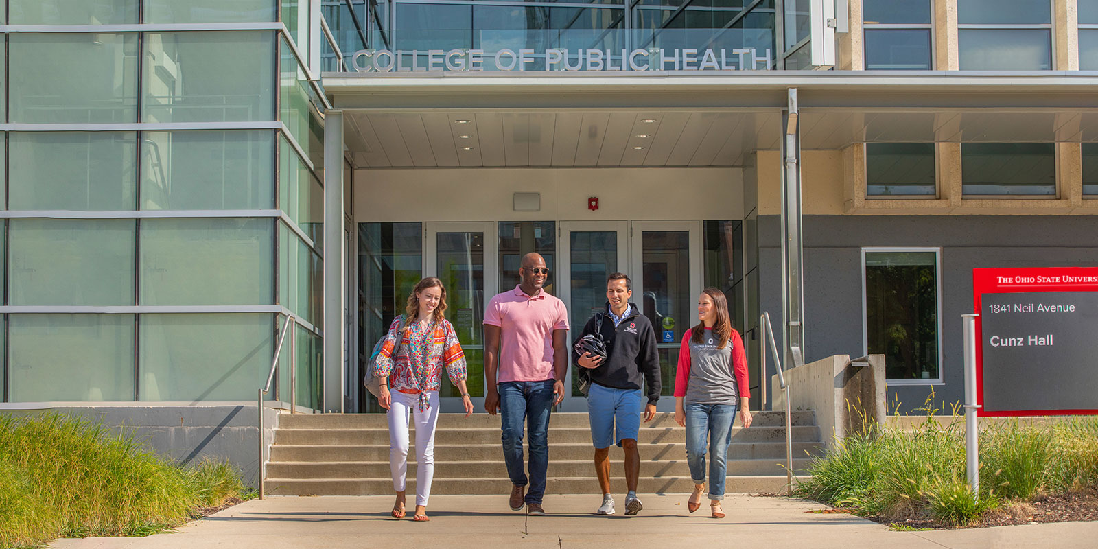 four people walking in front of Cunz Hall on a sunny day
